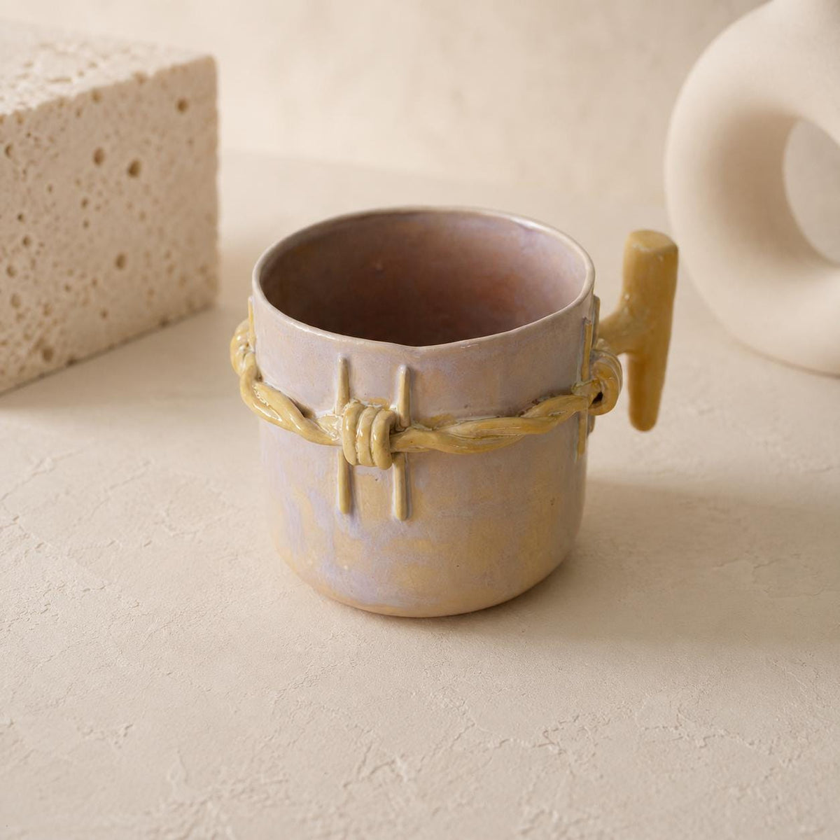 Raised twisted barbed-wire relief on a blush-beige ceramic mug