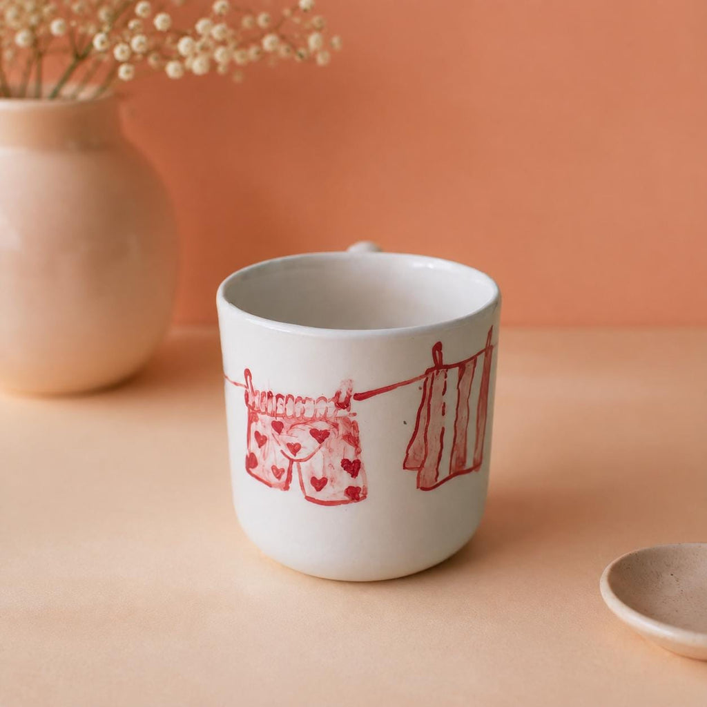 Red line drawing of hanging clothes on a white coffee mug