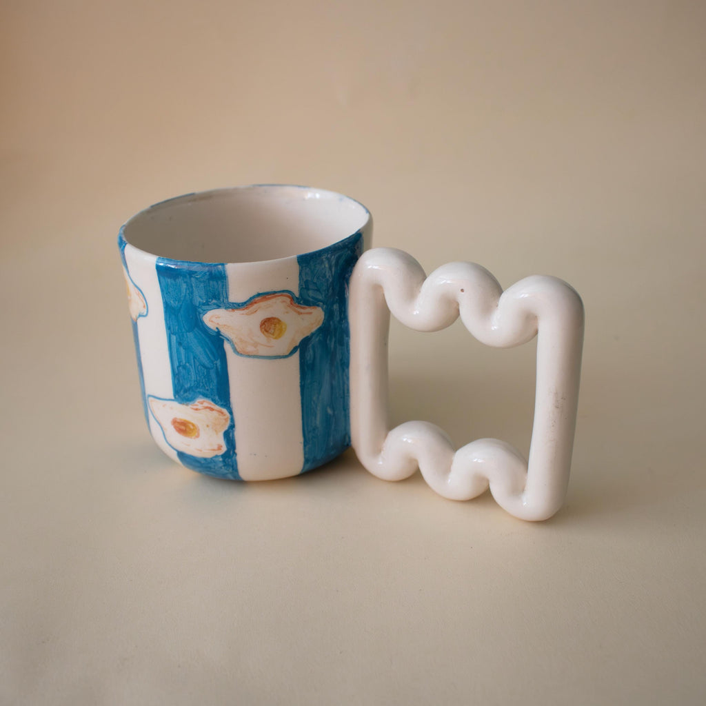 Fried egg motifs over vibrant blue stripes on a coffee mug